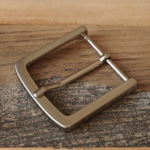 May include: A silver metal belt buckle with a smooth, polished finish.