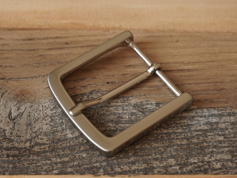 May include: A silver metal belt buckle with a smooth, polished finish.