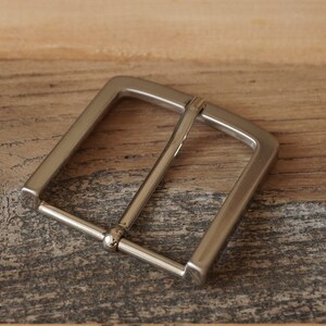 May include: A silver metal belt buckle with a rectangular shape and a smooth finish.