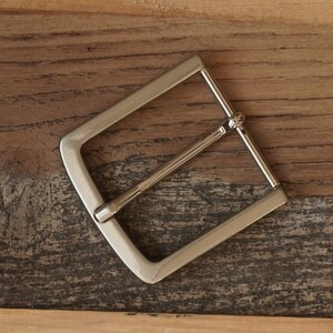 May include: A silver metal belt buckle with a rectangular shape and a smooth finish.