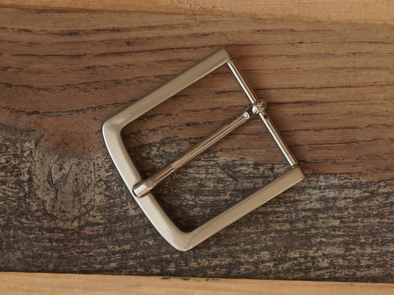 May include: A silver metal belt buckle with a rectangular shape and a smooth finish.