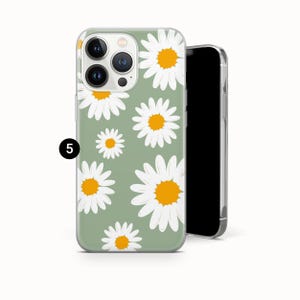 Pode incluir: Capa de telefone verde claro com um padr&atilde;o de margaridas brancas com centros amarelos. Um smartphone preto est&aacute; ao lado da capa.