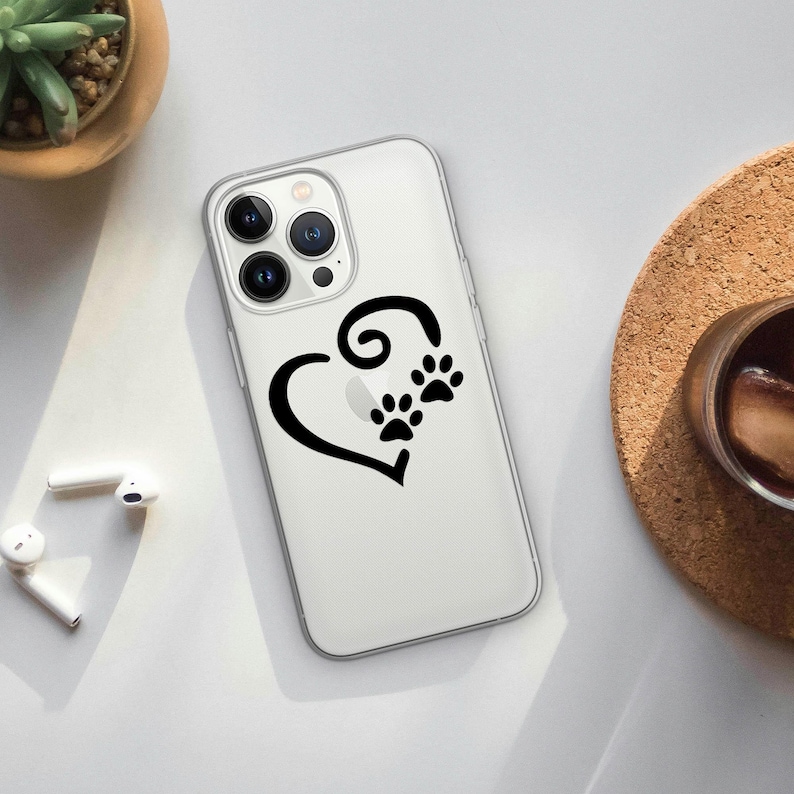May include: Clear phone case featuring a black heart design with paw prints. The case is made of a transparent material, allowing the phone's color to show through. The design is simple and elegant, perfect for pet lovers.