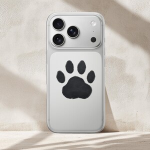 May include: Clear phone case with a black paw print design. The case has a clear border and a white backing with a large, black paw print in the center. The phone's camera lenses are visible at the top.