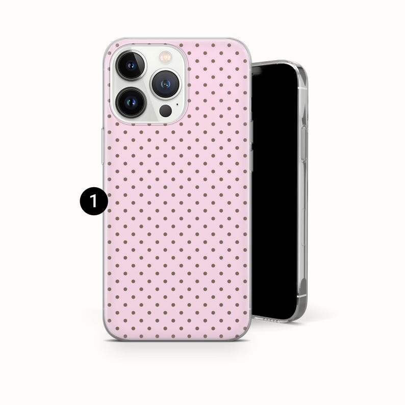 May include: A pink phone case with a repeating pattern of small, dark brown polka dots. The case is shown next to a black smartphone. The phone case has a camera cutout and button details.
