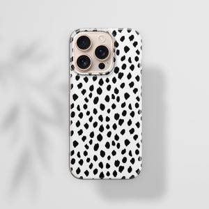 May include: A white phone case with a black dalmatian spot pattern. The case has a clear border and a camera module with multiple lenses. The background is a light gray surface with a shadow of leaves.