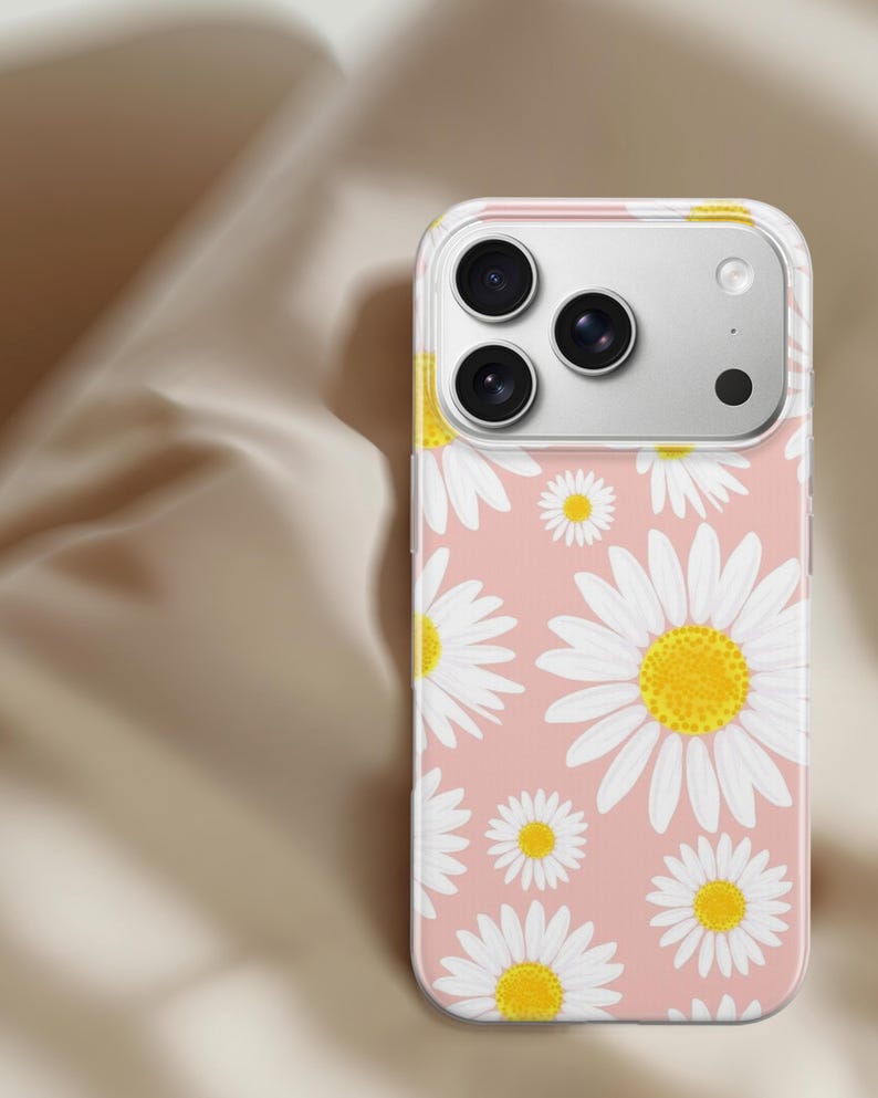 Pode incluir: Capa de telefone transparente com fundo rosa e um padr&atilde;o de margaridas brancas com centros amarelos. A capa cobre um telefone com tr&ecirc;s lentes de c&acirc;mera.
