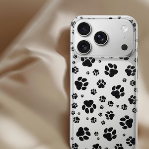 May include: Clear phone case with a black paw print pattern. The case has a transparent design with multiple black paw prints scattered across the surface. The phone's camera lenses are visible through the case.