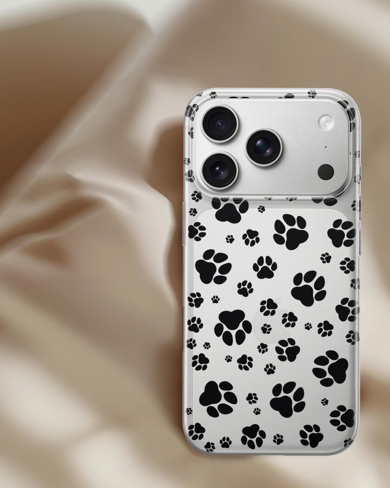 May include: Clear phone case with a black paw print pattern. The case has a transparent design with multiple black paw prints scattered across the surface. The phone's camera lenses are visible through the case.