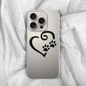 May include: A clear phone case featuring a black heart design with two paw prints. The case is shown on a white, textured fabric background. The phone case is designed to fit a smartphone.