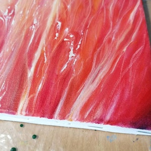 May include: Close-up of a red, orange, and white abstract painting on a canvas. The paint is applied in thick strokes, creating a textured surface.