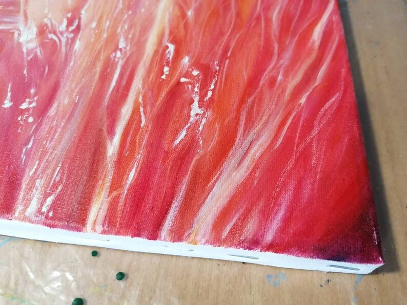 May include: Close-up of a red, orange, and white abstract painting on a canvas. The paint is applied in thick strokes, creating a textured surface.