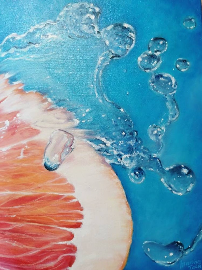 May include: A close-up of a grapefruit half submerged in water with bubbles rising to the surface. The grapefruit is a vibrant orange and red color, and the water is a bright blue.