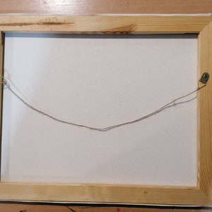 May include: The back of a wooden framed canvas painting with a string attached to two metal hooks for hanging.