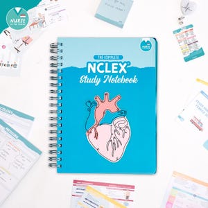 May include: A light blue spiral-bound notebook with the text "THE COMPLETE NCLEX Study Notebook" and a pink heart illustration. Study notes and a pin are scattered around the notebook, which is designed for nursing students.