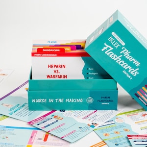 Puede incluir: Un juego de cajas turquesa de "NCLEX Pharm Flashcards, Edition 2" con una pila de tarjetas dentro. Las tarjetas est&aacute;n etiquetadas con t&eacute;rminos m&eacute;dicos como "Heparina vs. Warfarina" y "Cardiovascular". Otras tarjetas est&aacute;n esparcidas alrededor de la caja.