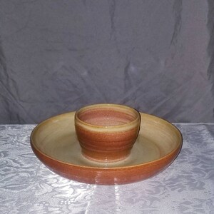 May include: A ceramic serving dish with a smaller bowl in the center. The dish is a light brown color with a darker brown rim. The bowl is a light pink color with a darker pink rim.