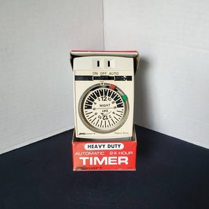 May include: A white heavy duty 24-hour automatic timer with a round dial and a green and red indicator. The timer is in a red and white box with the text "Heavy Duty Automatic 24 Hour Timer" on it.