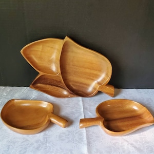 May include: Three wooden serving dishes in the shape of leaves. The largest dish is divided into three sections. The dishes are made of light brown wood.