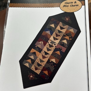 Könnte beinhalten: Ein Quiltmuster mit dem Titel "Heads or Tails" von Kansas Troubles Quilters. Das Muster zeigt ein geometrisches Design aus Dreiecken in verschiedenen Farben und Mustern. Der Name des Designers, Lynne Hagmeier, ist ebenfalls sichtbar.