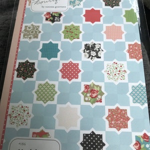 Puede incluir: Un paquete de patrones de edredón con un fondo azul claro y un diseño geométrico. Presenta bloques en forma de estrella en varios colores y patrones florales. El texto "Lella Boutique" y "Hubba Hubba" son visibles.