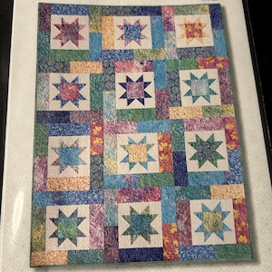 May include: A quilt pattern titled "LUCKY STARS" by Atkinson Designs. The quilt design features a repeating pattern of star blocks in various colors, including blue, green, pink, and yellow. The text "Fat Quarter Quilt" is also visible.