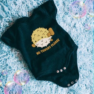 May include: Black baby onesie with a yellow and white pufferfish graphic and the text "NO TOUCHY PLEASE".
