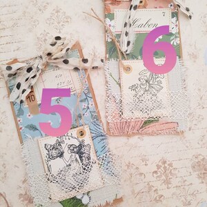 May include: Two handmade paper tags with a vintage aesthetic. The tags are decorated with lace, fabric scraps, and floral patterns. The top tag has the number "6" written on it in pink and the word "Calen" written on a smaller tag. The bottom tag has the number "5" written on it in pink. Both tags feature a black and white illustration of a fairy.