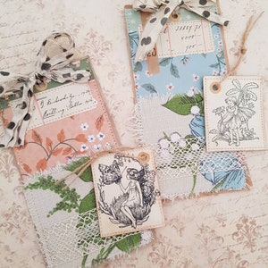 May include: Three handmade gift tags with a vintage aesthetic. The tags are decorated with floral patterned paper, lace, and fabric scraps. One tag features a black and white illustration of a fairy with a butterfly. The text on one tag reads "J. Reidschlager 1933 Notting Hill London 1933".