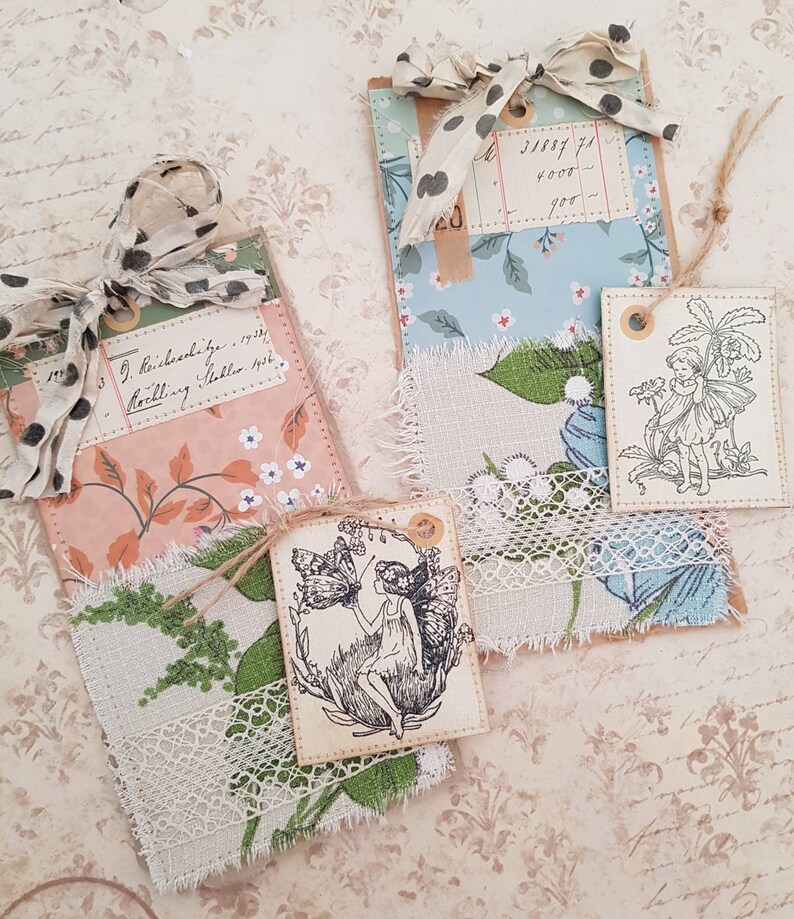 May include: Three handmade gift tags with a vintage aesthetic. The tags are decorated with floral patterned paper, lace, and fabric scraps. One tag features a black and white illustration of a fairy with a butterfly. The text on one tag reads "J. Reidschlager 1933 Notting Hill London 1933".