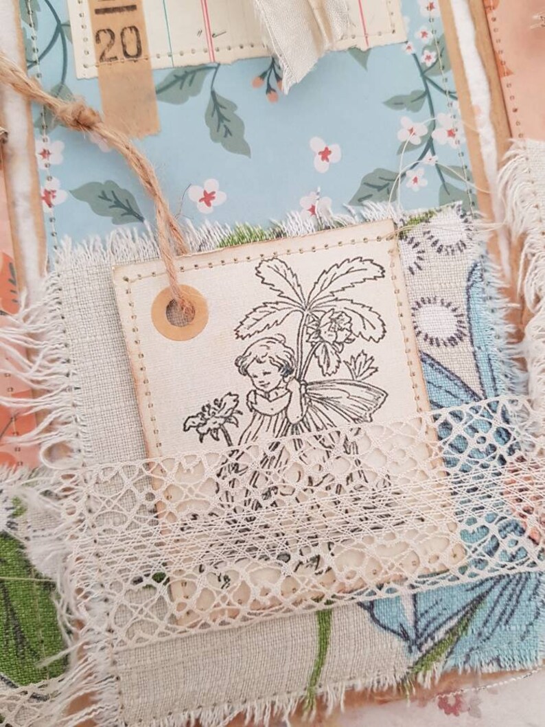 May include: A vintage-style fabric tag featuring a black and white illustration of a girl holding a flower. The tag is decorated with lace and has a brown circle with a hole in the centre.