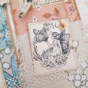 May include: A white tag featuring a black and white illustration of a fairy with a butterfly. The tag is tied with twine and has a brown circle around the hole.