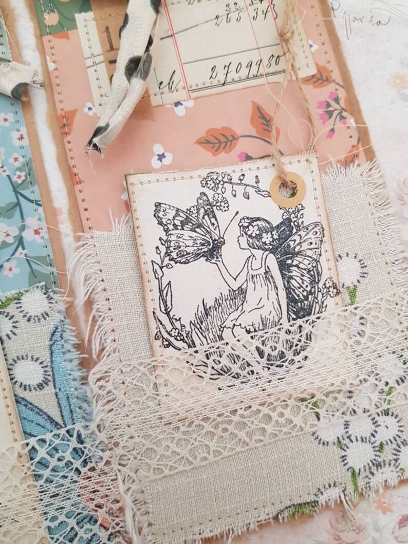 May include: A white tag featuring a black and white illustration of a fairy with a butterfly. The tag is tied with twine and has a brown circle around the hole.