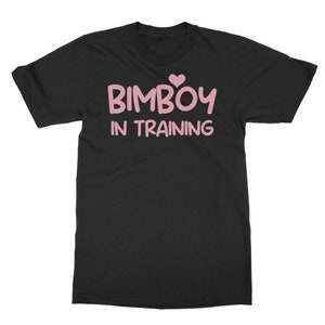 Peut inclure: T-shirt noir avec l'inscription rose "BIMBOY IN TRAINING", surmontée d'un cœur rose. Un vêtement décontracté, idéal pour un usage quotidien.