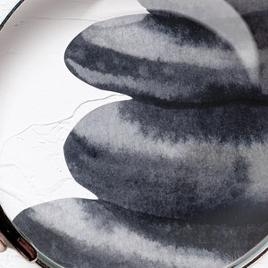 May include: A close-up of three gray and black watercolor painted stones stacked on top of each other. The stones are painted with a gradient of gray and black, and the edges are slightly blurred.