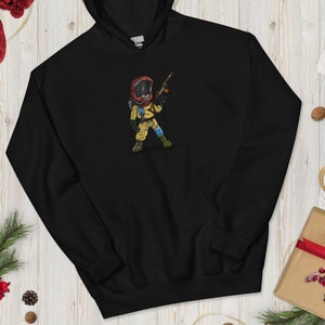 Puede incluir: Sudadera con capucha negra con una ilustración de dibujos animados de una persona con un traje de protección amarillo y una máscara de gas roja sosteniendo un arma.
