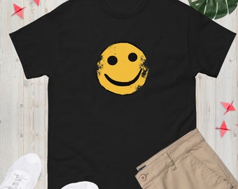 Könnte beinhalten: Schwarzes T-Shirt mit einem gelben Smiley-Motiv. Der Smiley hat einen abgenutzten, Vintage-Look.