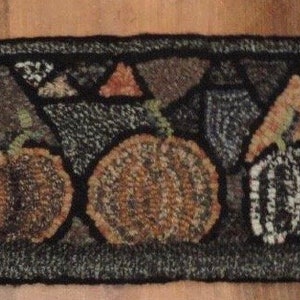 May include: A brown and black rug with a geometric pattern of pumpkins and leaves. The rug is made of wool and has a fringed edge.