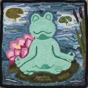 May include: A green frog sits in a meditative pose on a lily pad in a blue pond. The frog has closed eyes and is surrounded by a pink water lily and green reeds.