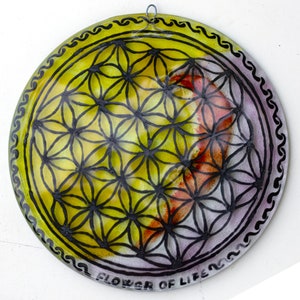 May include: A round, glass plate with a black and white geometric design of the Flower of Life. The plate has a yellow, orange, and purple background.