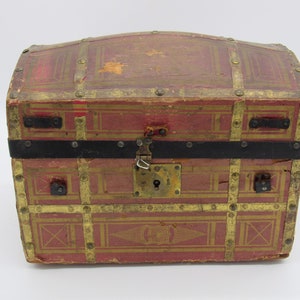 May include: A small, red wooden treasure chest with gold accents and a black metal latch. The chest has a decorative design on the front and is secured with metal studs.