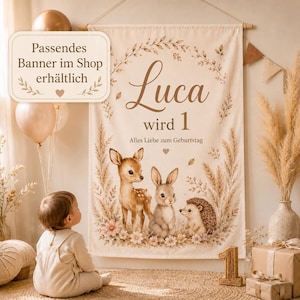 May include: A cream-colored fabric wall banner featuring the name Luca, the text wird 1, and Alles Liebe zum Geburtstag. The design includes illustrations of a fawn, a rabbit, and a hedgehog surrounded by pampas grass, leaves, and flowers.
