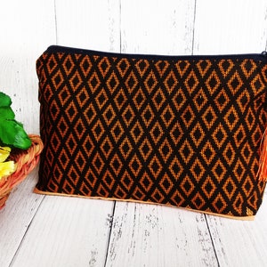 May include: A black and orange zippered pouch with a geometric pattern and a tassel. The pouch is made of fabric and has a zipper closure.