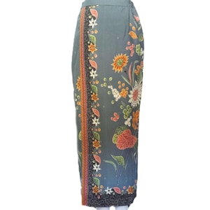 Puede incluir: Falda larga gris con estampado floral. La falda presenta un borde con detalles en naranja, negro y blanco. El diseño floral incluye flores naranjas, blancas y rosas con hojas verdes. La falda está hecha de una tela suave y fluida.