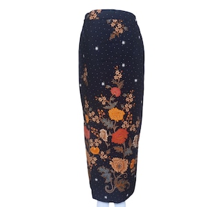 Puede incluir: Falda azul oscuro con estampado floral. La falda presenta un patrón repetido de pequeños puntos blancos y un gran diseño floral en tonos naranja, amarillo y marrón. La falda se exhibe en un maniquí blanco.