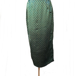 May include: A teal and gold patterned skirt displayed on a mannequin. The skirt has a geometric design and a straight silhouette. The fabric appears to be a satin or silk material. The skirt is knee-length.