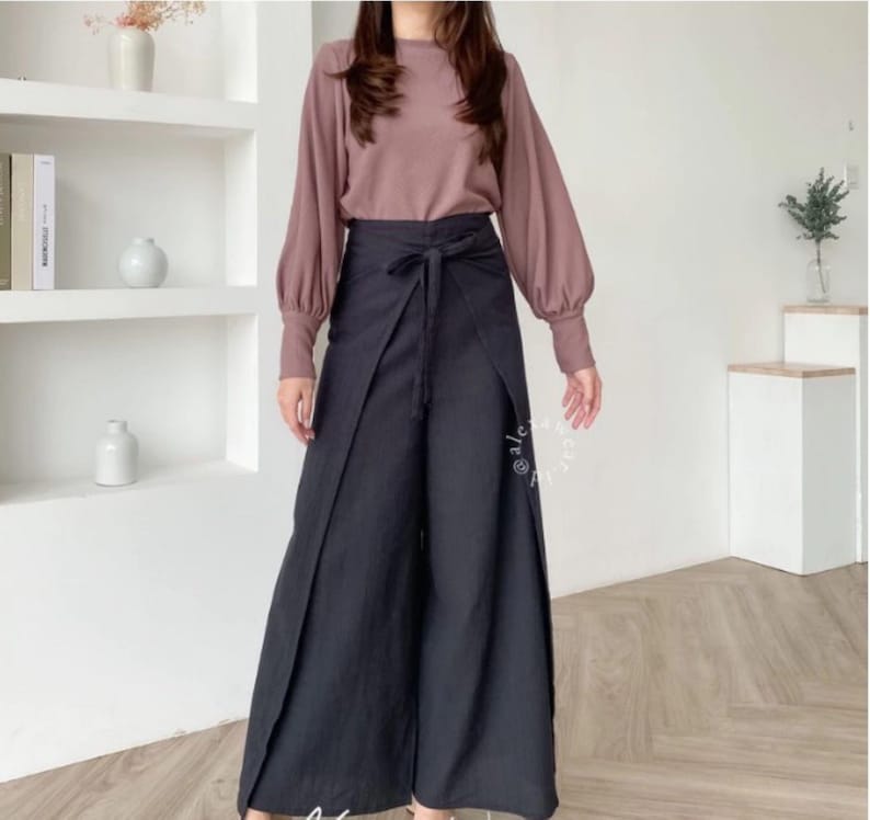 May include: A woman is wearing a long-sleeved, mauve blouse with a black wrap-style pant. The pants have a wide leg and a tie at the waist.