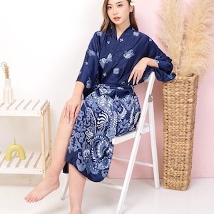 May include: A navy blue satin robe with a white floral pattern. The robe has a V-neck and long sleeves. The model is sitting on a white chair.