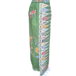 May include: Green batik pants with a floral and geometric design. The pants feature a repeating pattern of colorful triangles along the side and floral motifs. The fabric has a soft, flowing appearance.