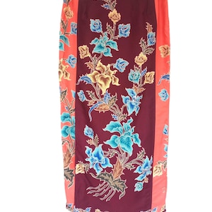 May include: A long skirt with a floral pattern. The skirt features a central panel of deep burgundy with blue, yellow, and white flowers. The sides are a coral color with matching floral accents. The skirt is made of a lightweight fabric.